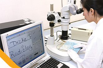 化驗師使用顯微鏡鑑辨文件真偽。