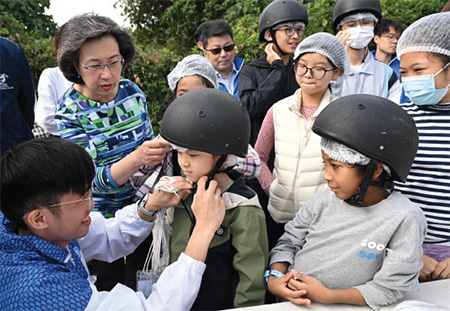 About 20 children from grassroots families visited the Tuen Mun Public Riding School in the company of civil service volunteers to sample the fun of horse riding. The Secretary for the Civil Service, Mrs Ingrid Yeung (second left), and volunteers from WSD helped a child get ready before the ride and another child enjoyed horse riding during the event.