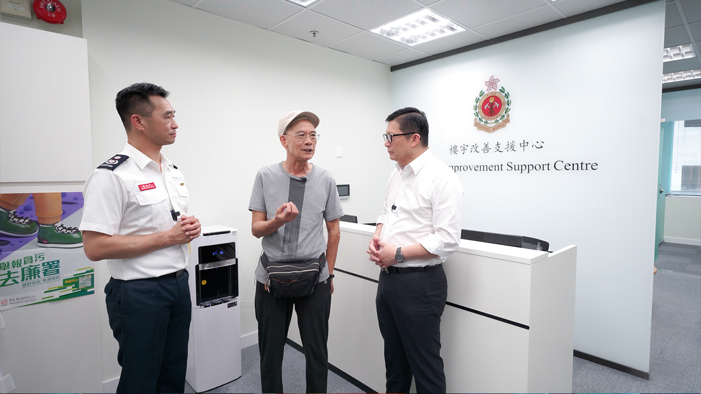 鄧局長(右)與時任消防處高級消防區長(樓宇改善策略辦公室)黃旭平先生(左)向市民介紹「消防處樓宇改善支援中心」的服務。   