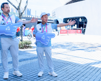 Volunteers from the Architectural Services Department held blue manicules printed with a sign of the Games at the plaza outside the Hong Kong Velodrome, showing spectators the way to the entrance of the venue for the track cycling events.  