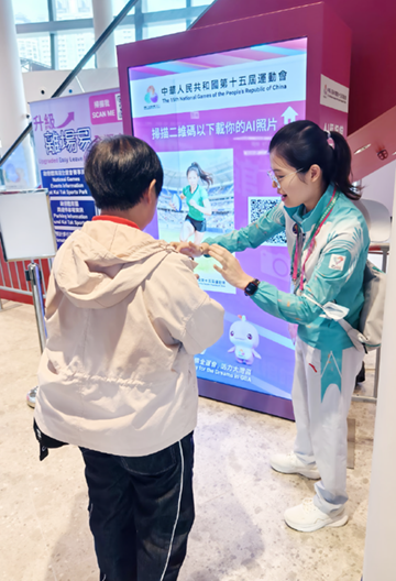During the rugby sevens competition, a volunteer from the Legal Aid Department assisted a spectator in downloading a competition-themed photo generated by artificial intelligence with an interactive device at the Kai Tak Stadium. 